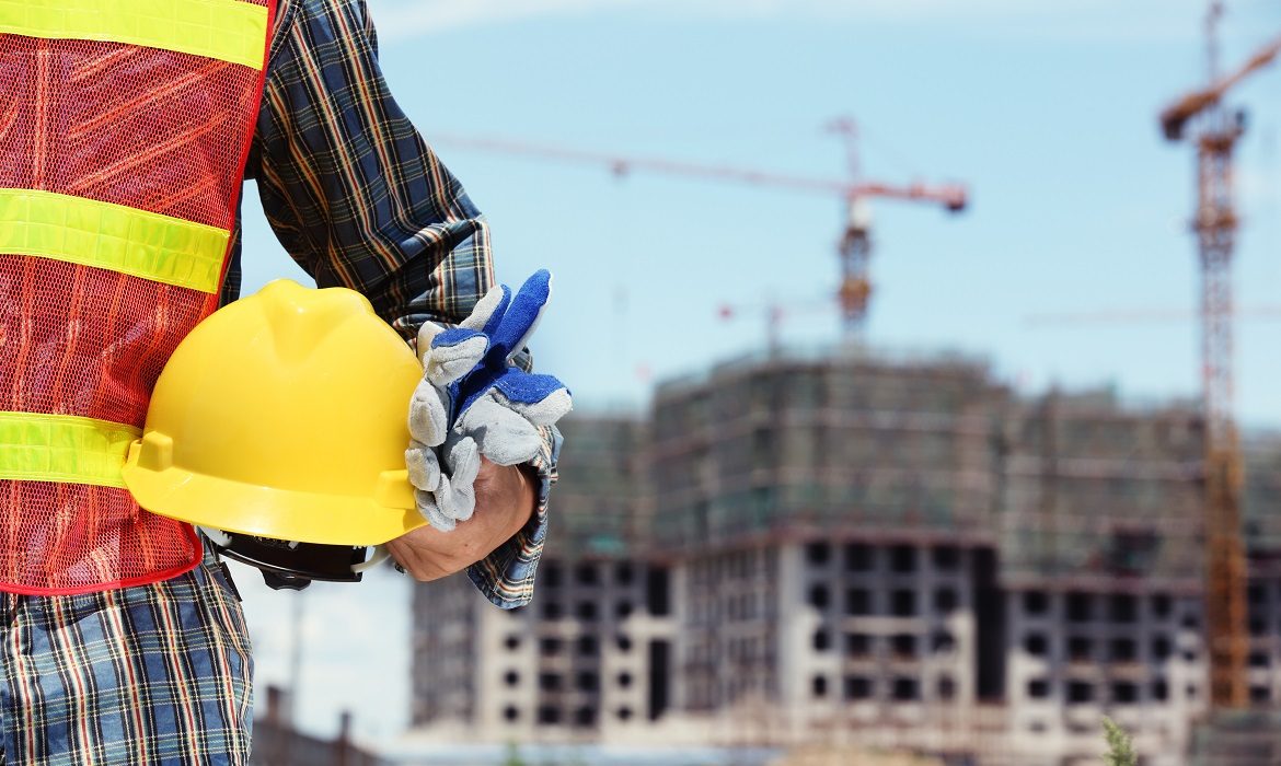 Man,Holding,Yellow,Helmet,In,Front,Of,Construction,Site